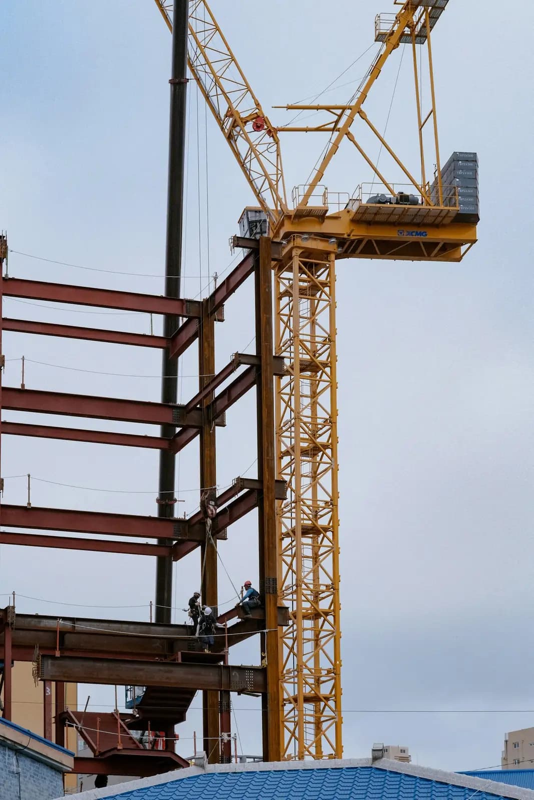 Steel frame of a building under construction, with workers and a tower crane